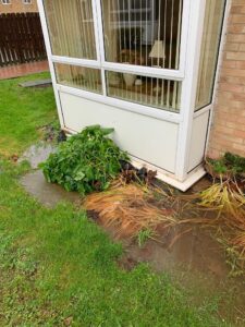 area outside a property with flooding. the flooding is under a window and has damaged surrounding plants