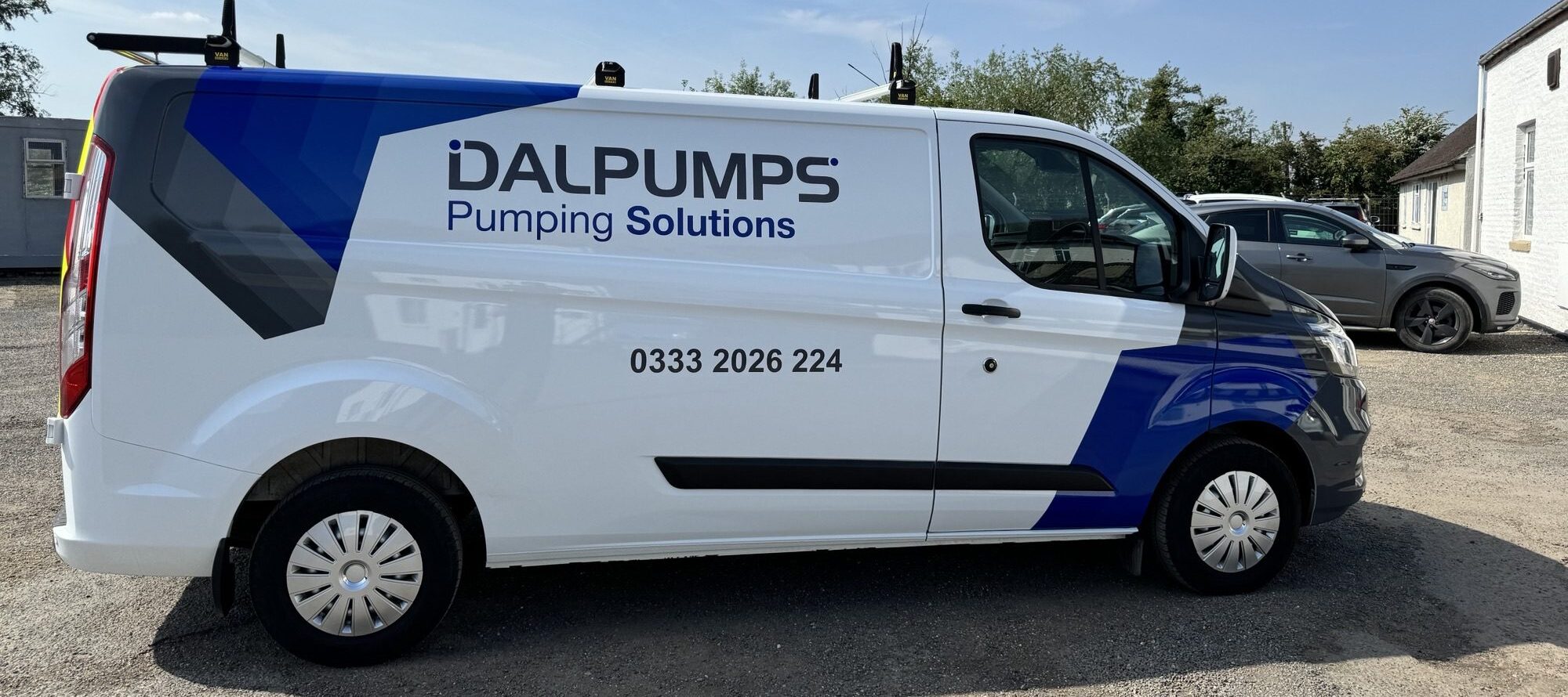 a white and blue van with "dalpumps" printed on the side in a car park. the sky is blue and bright